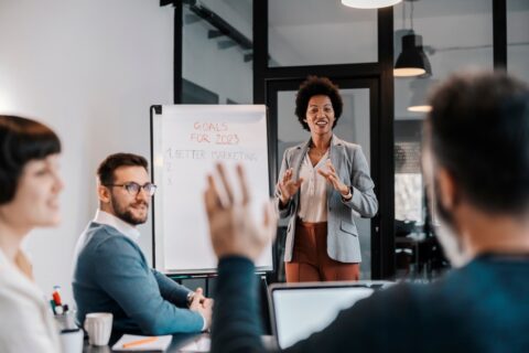 A interracial businesswoman is standing at the office with her team and brainstorming ideas for project.